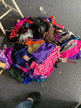 Load image into Gallery viewer, A large, unsorted pile of various dancewear items, including leotards, shorts, and embellished costumes, scattered on a grey carpeted floor.