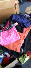 Load image into Gallery viewer, A cluttered pile of colorful dancewear, including a pink polka-dot leotard, a blue sports bra, and an orange top, resting in or near cardboard boxes.