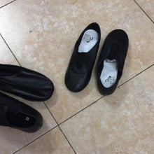 Load image into Gallery viewer, A pair of black slip-on leather dance shoes with white insoles placed next to other dance shoes on a tiled floor.
