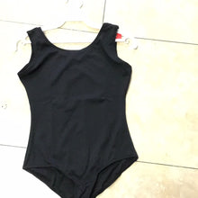 Load image into Gallery viewer, A simple black tank leotard displayed on a white plastic hanger against a tiled floor background.