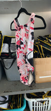 Load image into Gallery viewer, A sleeveless dance leotard with a pink, black, and white floral pattern, hanging on a black hanger in a storage area.