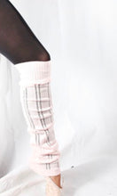 Load image into Gallery viewer, A dancer wearing light pink, ribbed knit leg warmers with subtle dark horizontal stripes, layered over black tights.