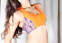 Load image into Gallery viewer, A close-up view of a vibrant orange dance crop top featuring contrasting purple lace side panels, worn by a dancer.