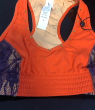Load image into Gallery viewer, A close-up product shot of an orange dance crop top with purple lace side panels, featuring a studded neckline and a tag attached to the racerback straps.