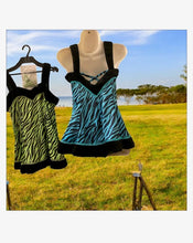 Load image into Gallery viewer, Ek lime green aur ek blue zebra-print dance dresses ki tasveer jismein black trim laga hua hai, jo ek mannequin par aur hanger par latki hui hain, ek khule maidan ke background mein.